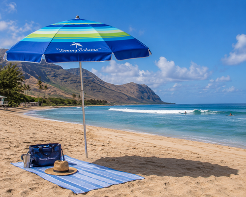 Beach scene with Tommy Bahama umbrella, towel, and hat on a sandy shore.